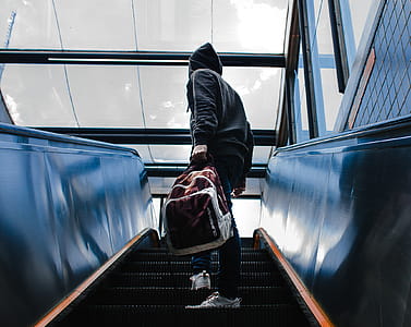 Person Wearing Black Hooded Jacket Standing on Escalator While Holding Backpack thumbnail