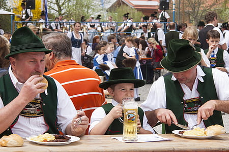 two men and one boy wearing green hat eating on brown wooden table thumbnail