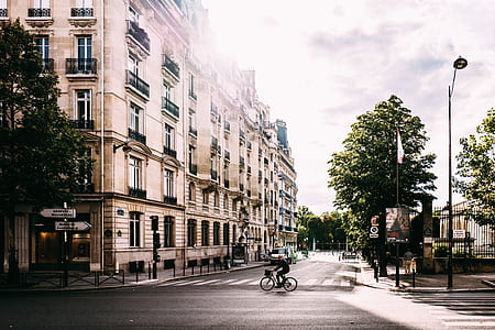 person riding on bike crossing road near beige building thumbnail