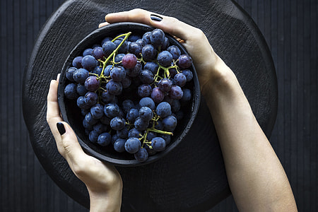 person holding bowl of grapes on round black wooden slab thumbnail