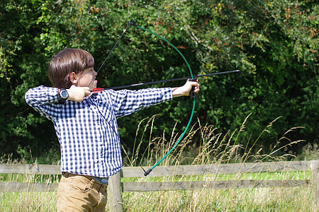boy in blue and white checked sport shirt holding crossbow thumbnail