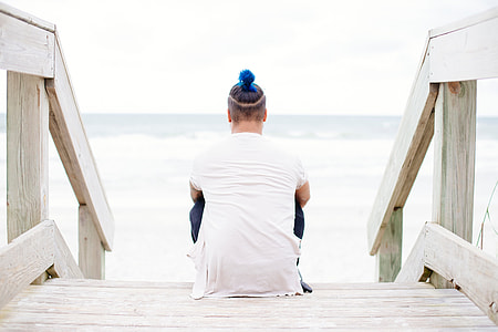 person in white top sitting on stair facing the body of water thumbnail