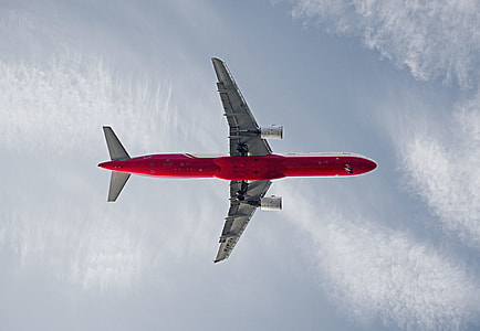 low-angle photography of red airplane flying under white clouds and blue sky thumbnail