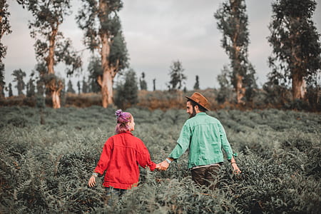 tilt-shift photography of man holding hands with woman walking on grass field thumbnail