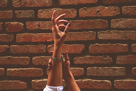 Person Wearing Watch and Rings Raising Left Hand Near Brick Wall thumbnail