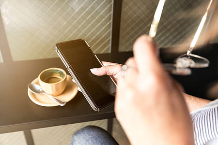 person holding smartphone near brown coffee cup with spoon thumbnail