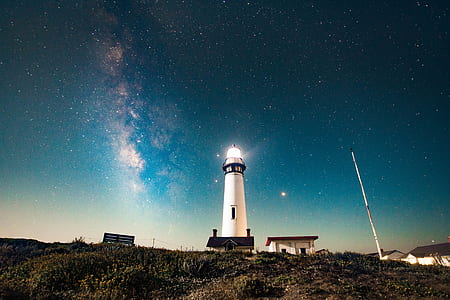white lighthouse between two houses on hill thumbnail