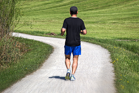 man jogging on gray pathway between grass fields photo thumbnail