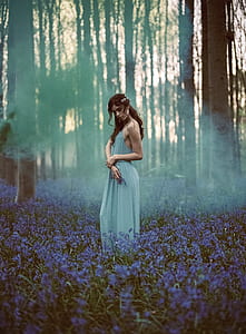 woman wearing gray spaghetti strap maxi dress in the middle of forest surrounded by blue petaled flowers thumbnail