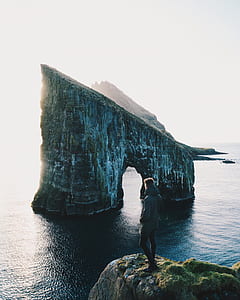 man standing on edge of rack facing on mountain rock thumbnail