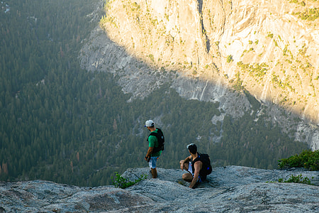 two men standing on rock ledge facing on cliff at daytime thumbnail