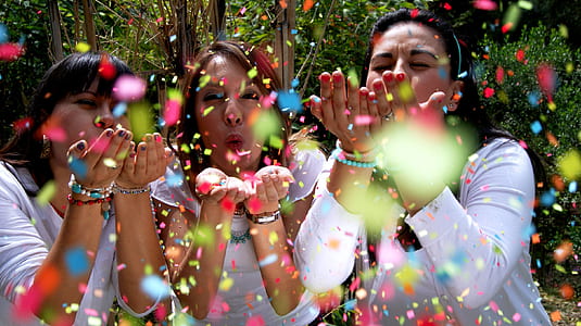 three woman blowing assorted-color confettis thumbnail