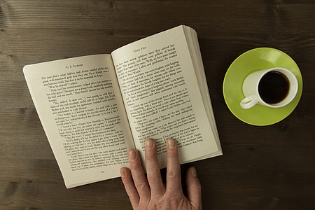 Overhead shot of a man reading a book with a cup of coffee on desk thumbnail