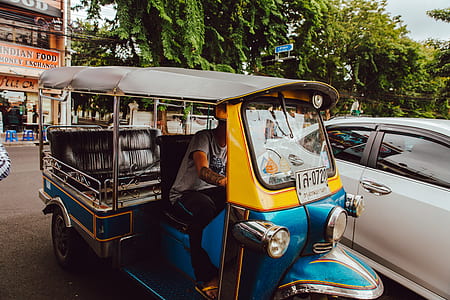 blue and yellow auto rickshaw near white car thumbnail