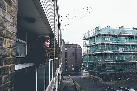 woman in brown coat leaning in balcony thumbnail