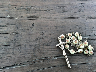 silver-colored and white rosary on brown wooden surface\ thumbnail