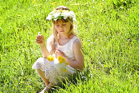 girl wearing white lace dress and flower crown sitting on green grass thumbnail