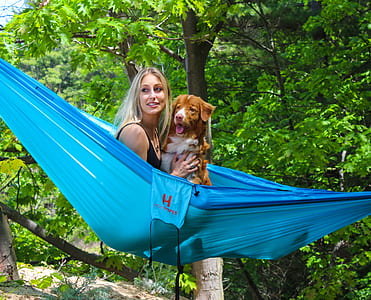 woman holding short-coated tan and white dog in blue hammock during daytime thumbnail
