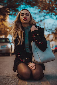 woman wearing black blazer and carrying gray leather bag kneeling in middle of street thumbnail