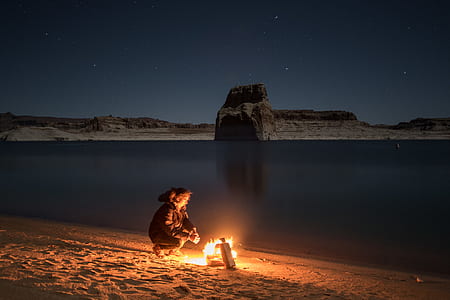 woman sitting on sand facing bonfire beside seashore thumbnail