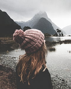 woman standing in front of calm body of water with mountain in distant under humid weather thumbnail