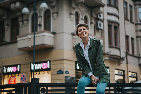 woman sitting on metal fence near concrete building thumbnail