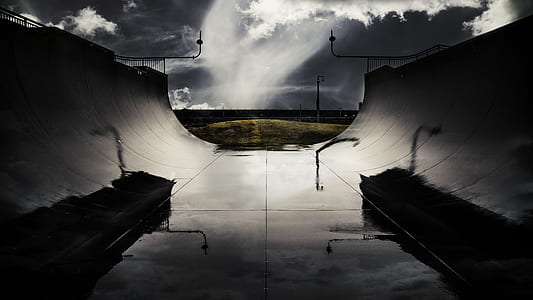 greyscale photography of skateboard stadium ramp near field under cloudy skies thumbnail