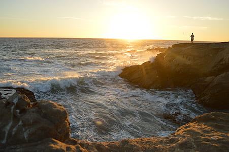 person standing on mountain cliff along body of water thumbnail