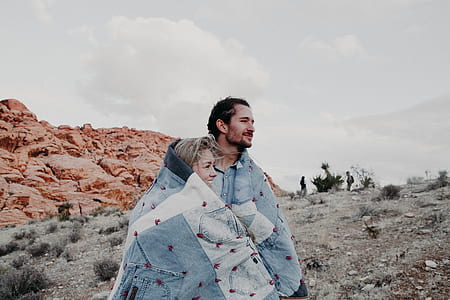 couple covered by blanket beside brown rock formation at daytime thumbnail