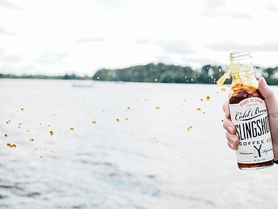 person holding coffee bottle near body of water thumbnail