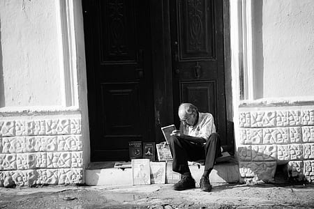 grayscale photo of man sitting on entrance displaying books thumbnail