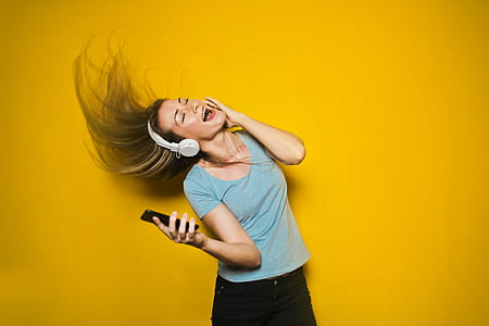 Excited woman dancing and listening music with headphones and smart phone with hair moving, isolated on yellow background thumbnail