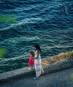 woman holding girl standing near body of water during daytime thumbnail