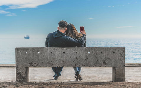 man and woman sitting on bench beside sea thumbnail
