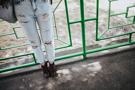 Blonde woman in a black jacket and ripped jeans by a green handrail thumbnail