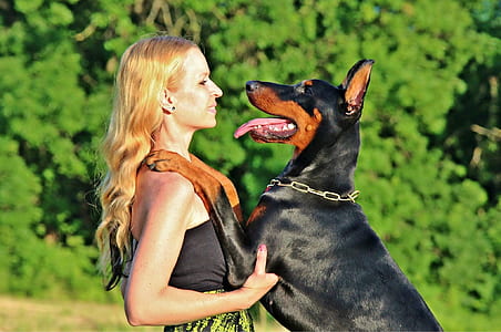 woman standing infront of black and tan Doberman pinscher near trees at daytime thumbnail