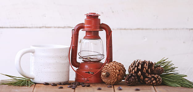 red kerosene lantern, white ceramic mug, and brown pine cones thumbnail