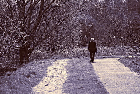grayscale photography of man talking on curved road near grass and trees thumbnail