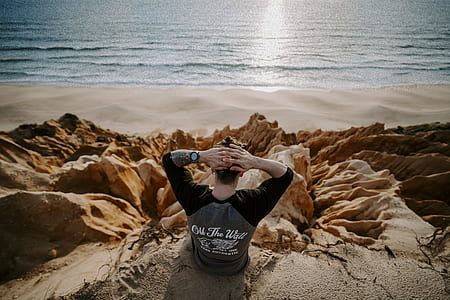 man sitting on rock formation near body of water thumbnail