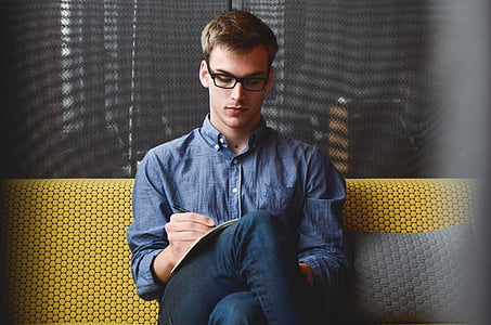 man sitting on yellow sofa white writing on paper thumbnail