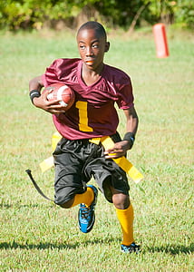 boy carrying football running on green grass field during daytime thumbnail