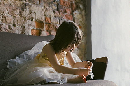 Girl in Yellow-and-white Dress Sitting on Couch While Holding Her Foot thumbnail
