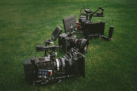 three black professional video cameras on green grass field thumbnail