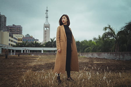 standing woman wearing brown coat under grey sky thumbnail