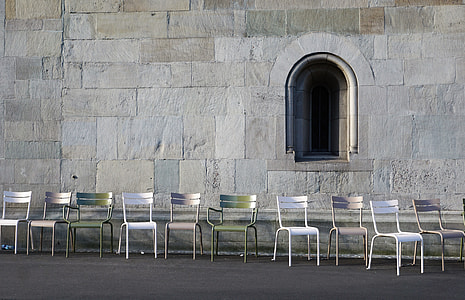 empty row of metal armless chairs on side of gray wall at daytime thumbnail