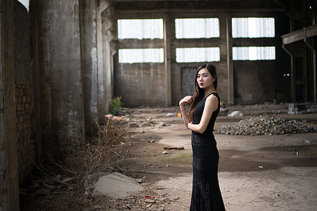 woman in black sleeveless sheath dress standing near concrete wall thumbnail