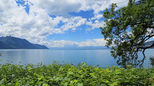 calm body of water near mountains under white clouds thumbnail