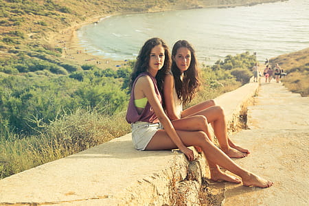 Two young brunette women in casuals sitting on the rock stairway near a beach thumbnail