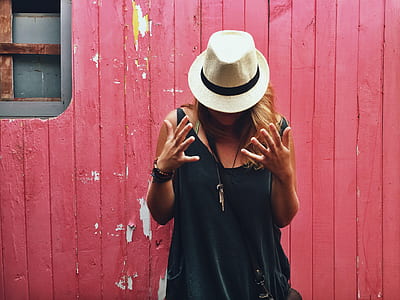 woman wearing white and black fedora hat standing near red wooden wall thumbnail