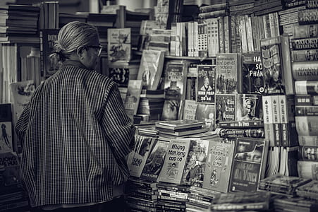 Person Standing in Front of Assorted Books in Gray Scale Photography thumbnail